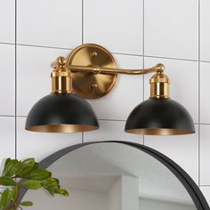 two black and gold lights on a white tiled wall next to a potted plant