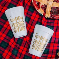 two cups that say happy friends giving sitting on a plaid blanket next to a pie