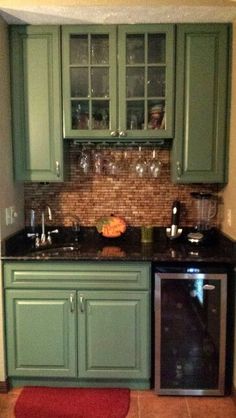 a kitchen with green cabinets and black counter tops, red rug on the floor in front of it