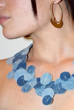 a close up of a person wearing a necklace with blue flowers on it and gold hoop earrings