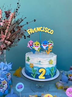 a blue and white cake sitting on top of a table next to cupcakes