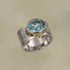 The 'Garbo' ring is a gorgeous statement ring set with a large natural blue topaz stone. The bezel is 18K gold vermeil adding a luxurious warmth to the lovely textured band of solid silver. Be prepared for admiring looks! Sterling silver 18K gold vermeil Natural Blue Topaz Width: 10 mm This ring comes in 4 sizes:  L (US 6) N (US 7) P (US 8) S (US 9)  U (US 10) NOTE: When ordering a wide ring we reccomend going up a size from your normal ring size. All of our sterling silver jewellery comes beaut Luxury Large Stone Silver Topaz Ring, Modern Topaz Ring With Gemstone Accents For Anniversary, Blue Topaz Rings With Bezel Setting, Mother Of The Bride Jewelry, Wide Silver Band, Blue Topaz Stone, Topaz Gemstone, Solitaire Ring, Silver Band