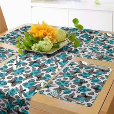 a dining table with blue and white flowers on it, next to a bowl of green leaves