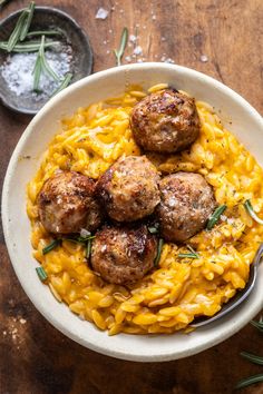 a bowl filled with pasta and meatballs on top of a wooden table next to two spoons