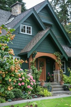 a green house with lots of flowers in the front yard and steps leading up to it