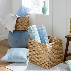 three baskets filled with blue and white pillows on top of a wooden floor next to a window