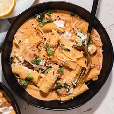 two black bowls filled with pasta and cheese on top of a table next to slices of lemon