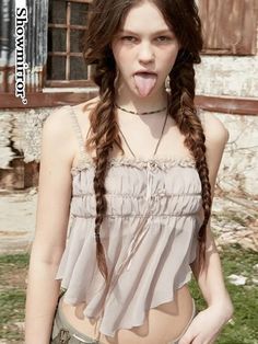 a woman with long hair sticking out her tongue in front of an old building and grass