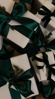 many white boxes with green bows and pine branches on them are wrapped in satin ribbon