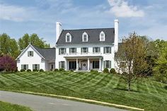 a large white house sitting on the side of a lush green field next to a road