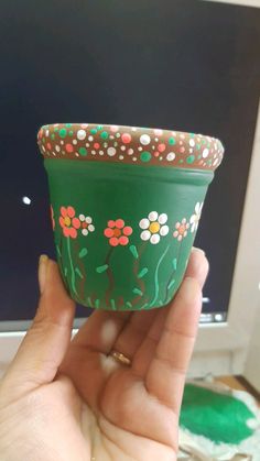 a hand holding a green flower pot with flowers painted on the side and dots around the rim