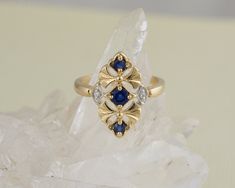 This elegant vintage ring features three blue sapphires set in a row. The rich yellow gold is a perfect back drop for this elongated style ring. Two sparkling diamonds accent the sides.  Normal Price: $895.00 Metal: 14k Yellow Gold Gemstone Type: Diamond, Sapphire Gemstone Shape: Round  AA Sapphire: 0.56 ctw total karat weight Diamond: G-H color, Si clarity, 0.01 tdw total diamond weight Design Elements: diamond ring, floral design, sapphire  Condition: Estate - may show some signs of wear due t Gold And Sapphire Jewelry, Sapphire And Diamond Ring, Graduation Rings, Blue Stone Ring, Sapphire Jewelry, Gems Jewelry