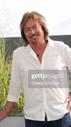 a man standing next to a planter with his hands in his pockets and smiling