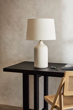 a white lamp sitting on top of a wooden table next to a chair and desk