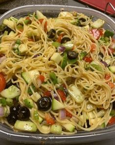 a bowl filled with pasta, olives and cucumbers on top of a table