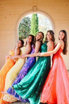 four women in long dresses posing for the camera with their arms around each other and smiling