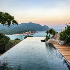 an outdoor swimming pool surrounded by trees and water with mountains in the background at dusk