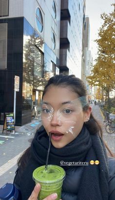 a woman holding a green smoothie in front of her face