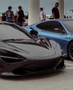 two sports cars parked next to each other in a parking lot with people standing around