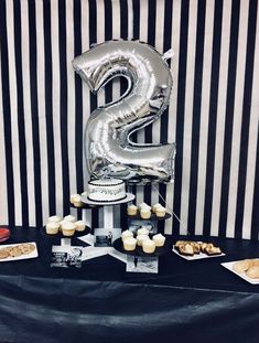 a black and white table topped with cupcakes next to a number 3 balloon