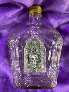 a glass bottle with an image on the front and bottom, sitting on a purple cloth