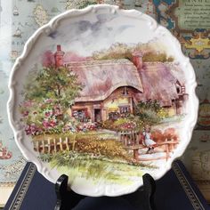 a plate with a painting of a cottage on the front and side, sitting on a table