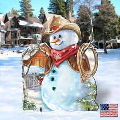 a snowman wearing a cowboy hat and scarf next to a house in the snow