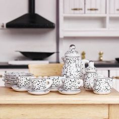 a wooden table topped with cups and saucers next to a stove top covered in white dishes