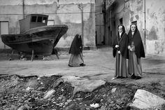 two women standing in front of a boat on the beach, one wearing a nun outfit