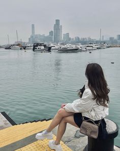 a woman sitting on top of a pole next to the ocean with boats in the background