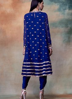 Step into elegance and grace with our Deep Blue High Low Kurta Set. This stunning Indo indo western ensemble features a double-tiered kurta in a deep blue hue. The intricate embellishments add a touch of opulence, while the high-low design adds a modern twist. Complete the look with the beautiful dhoti set with gold detail Embrace the perfect blend of traditional and contemporary style with this Indo western masterpiece. Composition : Kurta - Georgette, Dhoti and Inner - Crepe Care: Dry Clean Only and Vacuum Storage This product can be customized for sleeves, length of blouse and neckline Delivery : 6-8 weeks as the product is hand crafted. Check Size Guide or choose MySize for free customisation (All Sizes above XL can be made at 15% additional cost) For more information and sizes please High Low Kurta, Kurta With Dhoti, Ruffled Saree, Vani Vats, Set Saree, Saree Gown, Dhoti Pants, Drape Saree, Indian Wedding Wear