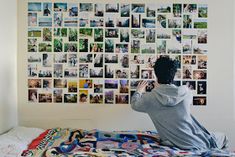 a man sitting on top of a bed in front of a wall covered with pictures