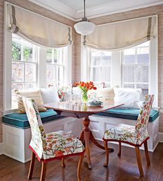 a dining room table with two chairs and a bench in front of the bay window