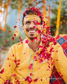 a man in yellow with red petals on his face and chest is smiling at the camera