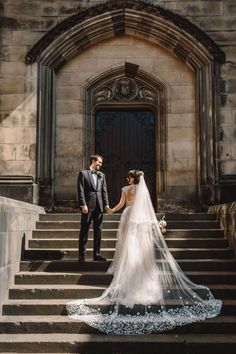 a bride and groom standing on the steps of an old building holding each other's hands