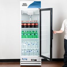 a man standing next to a refrigerator filled with water and soda bottles in front of a white wall