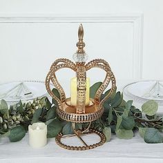 a crown shaped candle holder on a table with greenery and candles in front of it