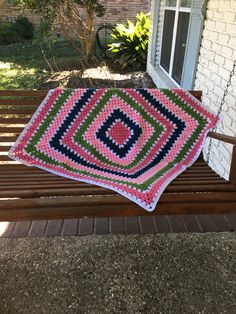 a crocheted blanket sitting on top of a wooden bench next to a brick building