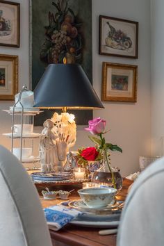 a dining room table with plates, cups and flowers on it next to a lamp