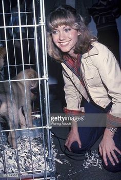 a woman is posing in front of a cage with a small animal behind her,