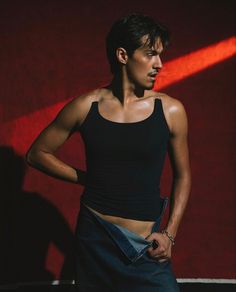 a young man is posing in front of a red wall with his hands on his hips