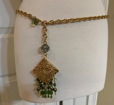 "Vintage Angelo Marani Italy shiny gold chain belt with an ornate gold filigree medallion, faux pearl and rhinestone fringe, and a rhinestone embellished ball. The belt measures 41\" from the top of the chain to the decorated ball. At the end of the chain hangs a gold and green rhinestone ball followed by an ornate gold carved pendant which attaches the rhinestone and faux pearl tassels. The belt has a large lobster clasp and a round Angelo Marani tag. The pendant has 4 rows of hanging fringe on Rihnestone Belt, Bohemian Gold Chain Belt With Adjustable Chain, Bohemian Gold Chain Belt, Bohemian Gold Chain Belt Gift, Bohemian Gold Chain Belt As A Gift, Bohemian Gold Chain Belt - Perfect Gift, Bohemian Gold Chain Belt - Perfect As A Gift, Pearl Tassels, Pearl Fringe