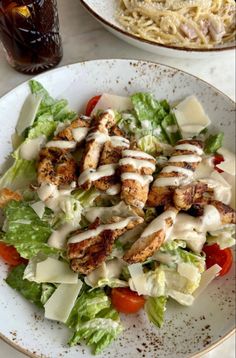 a salad with chicken and dressing on it sitting next to a bottle of soda in a white bowl