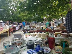 an outdoor flea market with lots of items on the table and people standing around it