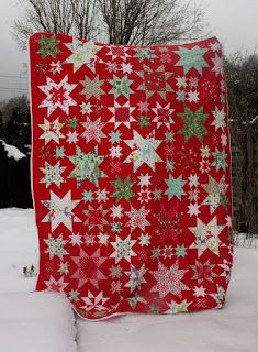 a red and white quilt sitting on top of snow covered ground next to a tree