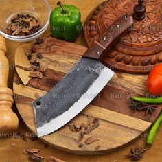 a large knife sitting on top of a wooden cutting board next to vegetables and spices