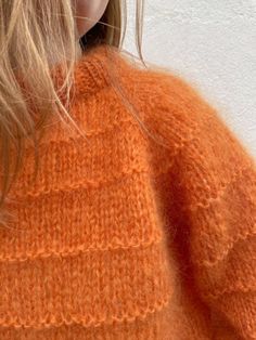 the back of a woman's orange sweater, with her hair blowing in the wind