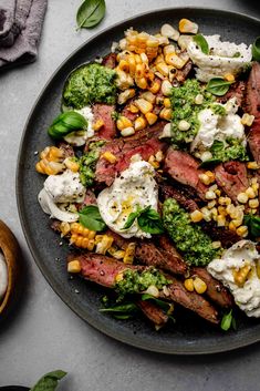 a plate with corn, broccoli and meat on it next to a spoon