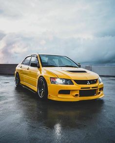 the yellow car is parked on the wet parking lot in front of an overcast sky