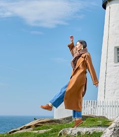 a woman standing on top of a grass covered hill next to a lighthouse with her arms in the air